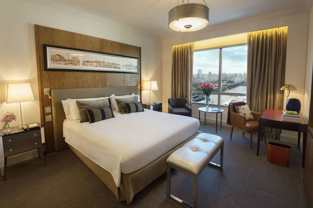 Une chambre d’hôtel avec un grand lit, un bureau, une chaise, une petite table et une vue sur la ville.
