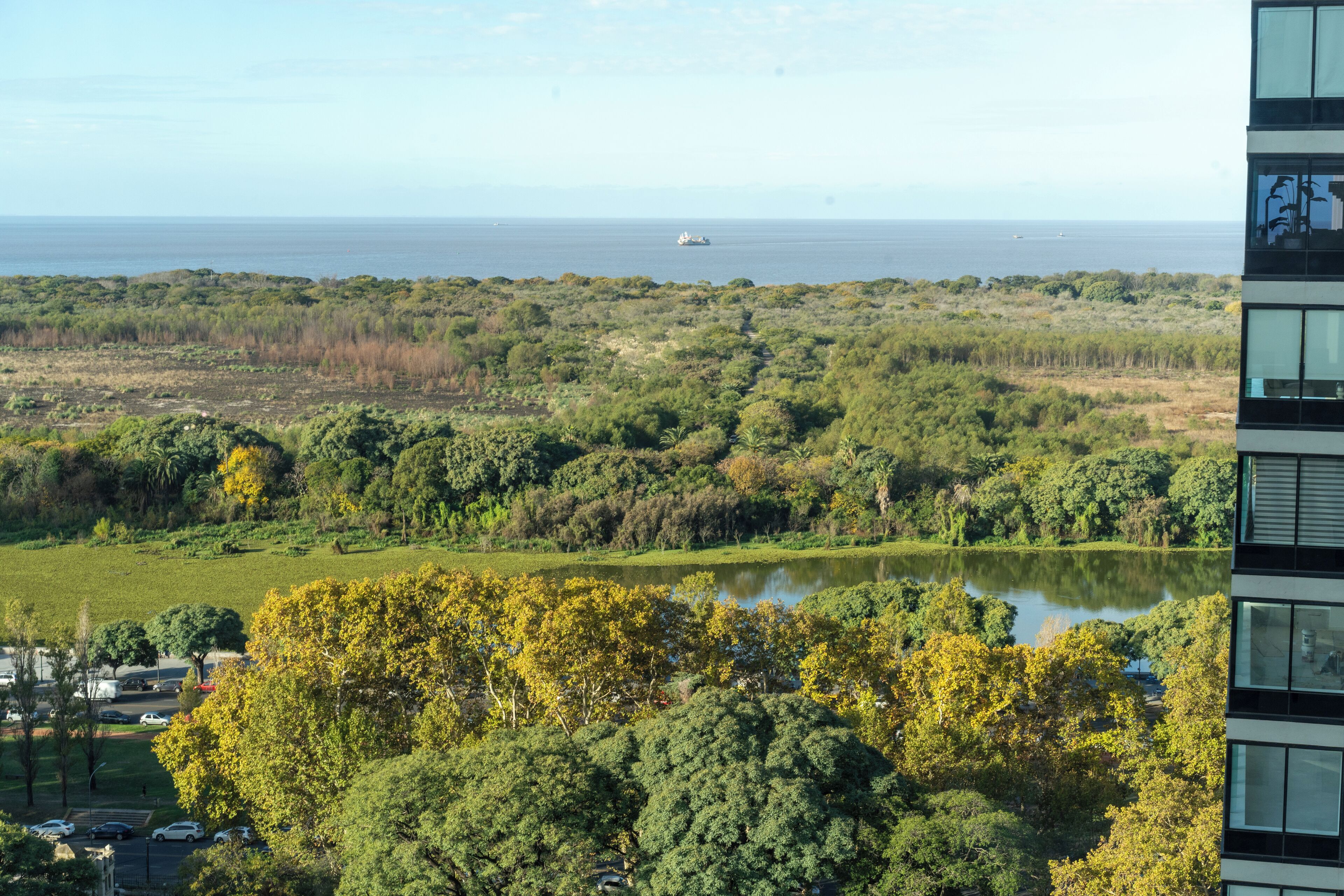 A view of a lake surrounded by dense greenery and a distant ship on the water.