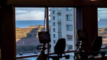 Vista desde una habitación con bicicletas estáticas, que da a una zona costera con un edificio y vegetación.