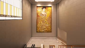 A modern interior with a large mosaic artwork on the wall, a staircase with a wooden handrail, and a glass railing on the left.