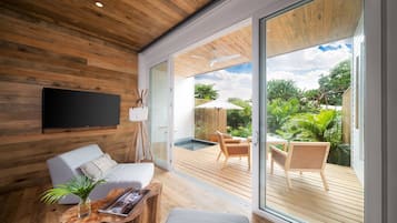 A modern living room with a wooden ceiling, a flat-screen TV, a sofa, a coffee table, and a view of an outdoor deck with a pool and chairs.
