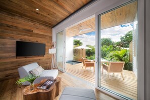 A modern living room with a wooden ceiling, a flat-screen TV, a sofa, a coffee table, and a view of an outdoor deck with a pool and chairs.