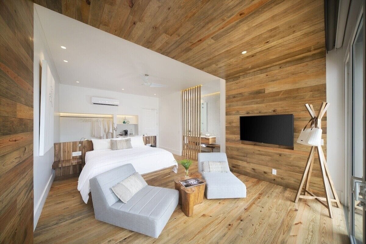 Ein modernes Schlafzimmer mit einem großen Bett, zwei Sessel, einem Fernseher und Holzboden.