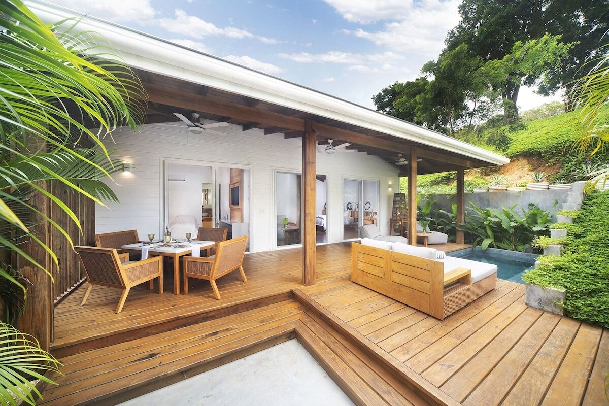 Um deck de madeira com piscina, área de estar externa e um espaço coberto com ventilador de teto.
