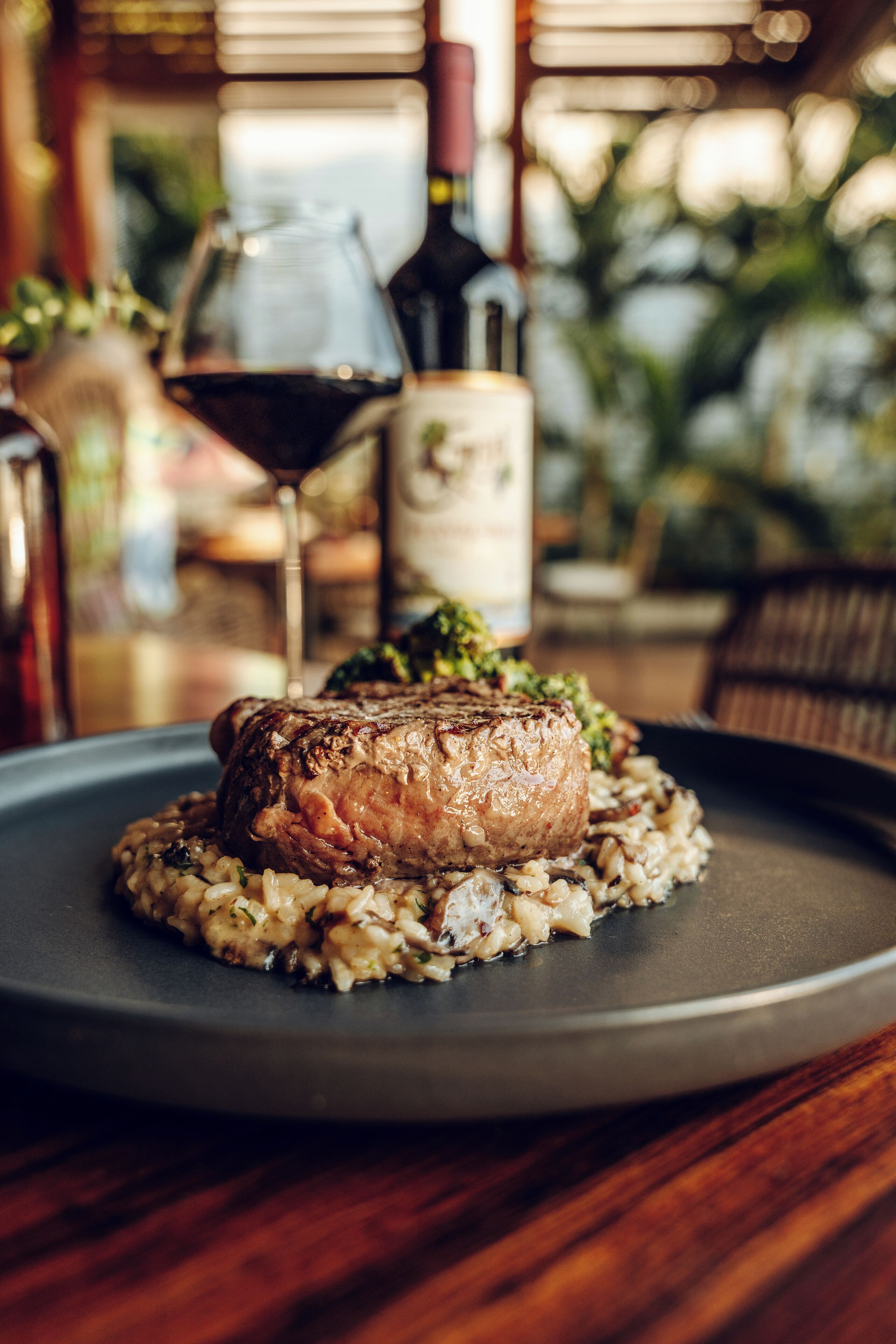 A plate with a steak and risotto, a wine glass, and a bottle of wine on a table.