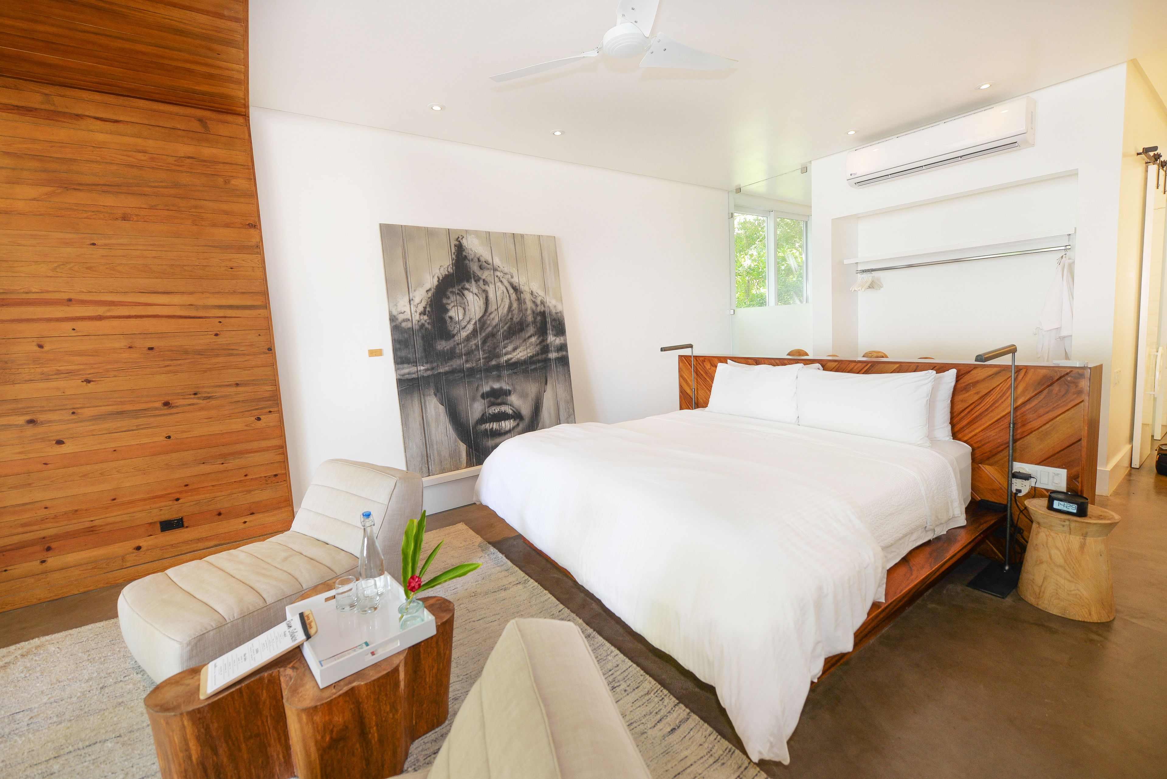 Un dormitorio moderno con una cama grande, cabecera de madera, una mesita de noche, una silla y un cuadro abstracto de gran tamaño en la pared.