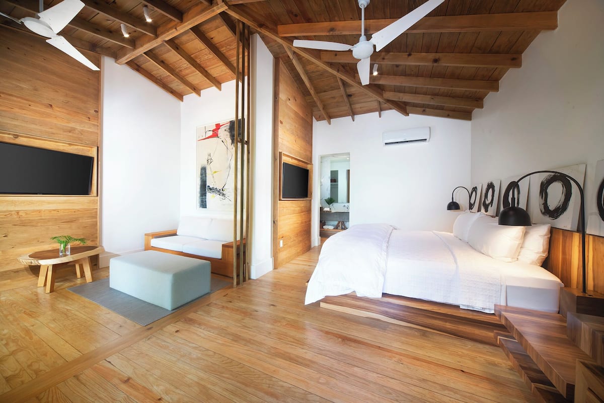 Ein modernes Schlafzimmer mit Holzboden, einem Bett, einer kleinen Sitzecke und einem an der Wand montierten Fernseher.