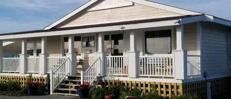 A single-story building with a gabled roof, a front porch with white railings, and a small staircase leading to the entrance.