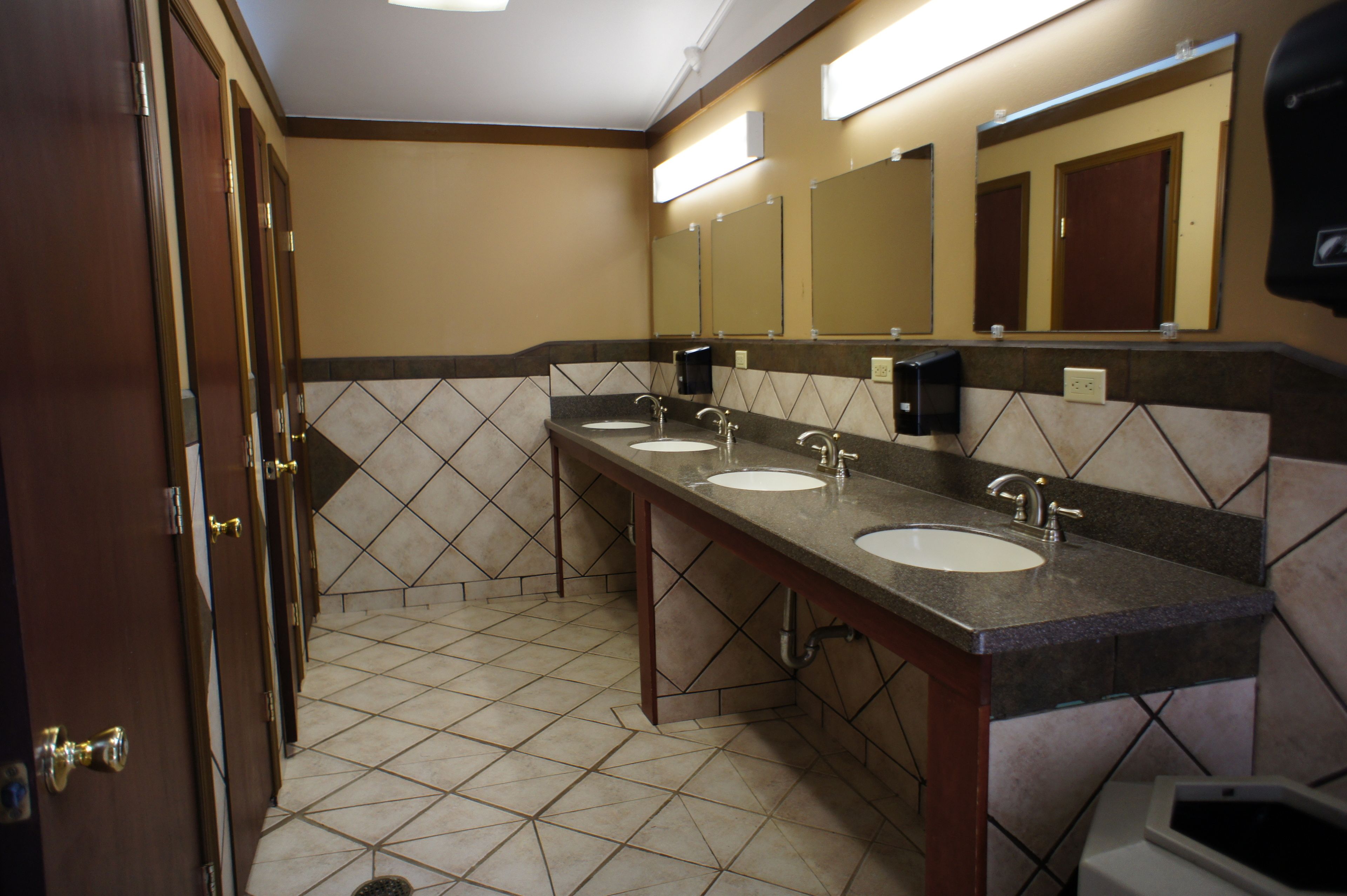 A public restroom with three sinks, a hand dryer, and a trash can.