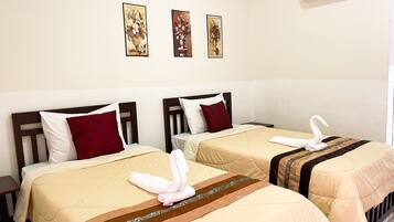 A hotel room with two beds, each with a red and white pillow, beige bedding, and a decorative towel on the bed. There are three wall-mounted paintings above the beds.