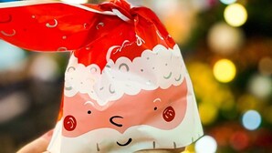 A hand holding a Santa Claus-themed gift bag with a red ribbon.