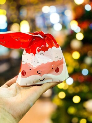 A hand holding a Santa Claus-themed gift bag with a red ribbon.