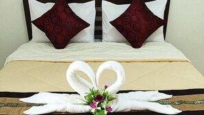 A neatly made bed with a heart-shaped towel arrangement and a small vase of flowers.