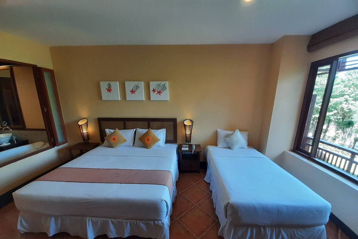 A hotel room with two beds, a large window, a mirror, and artwork on the wall.
