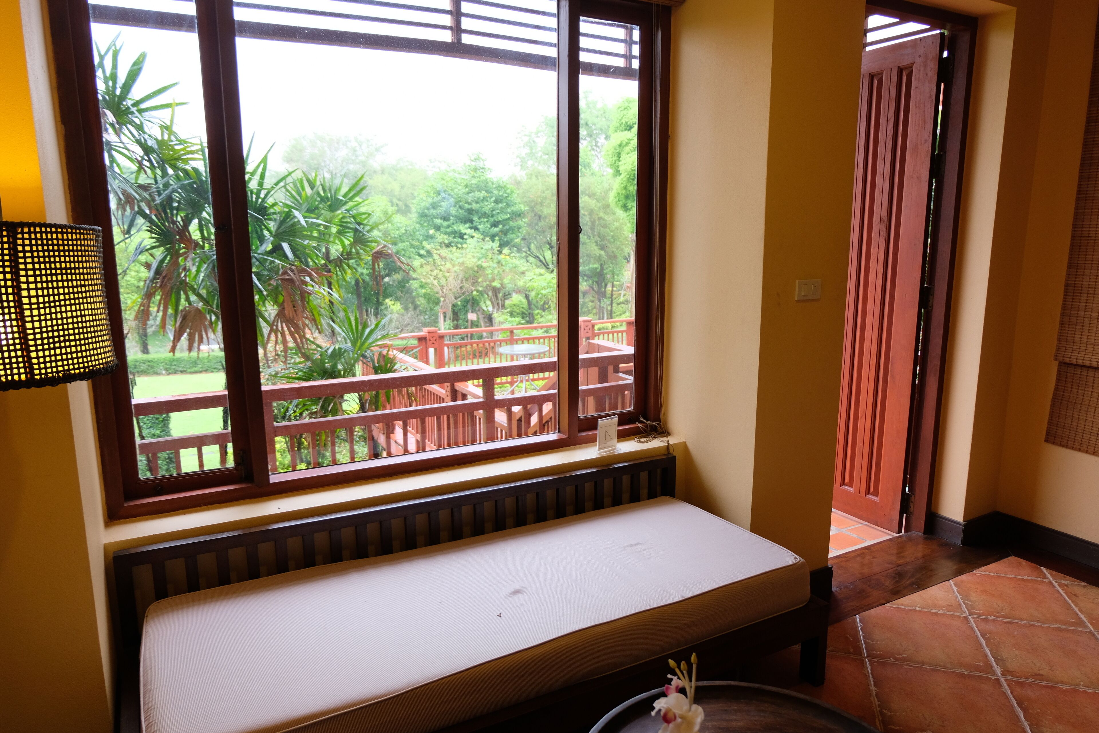 A room with a window overlooking a garden, a bench, and a door leading outside.
