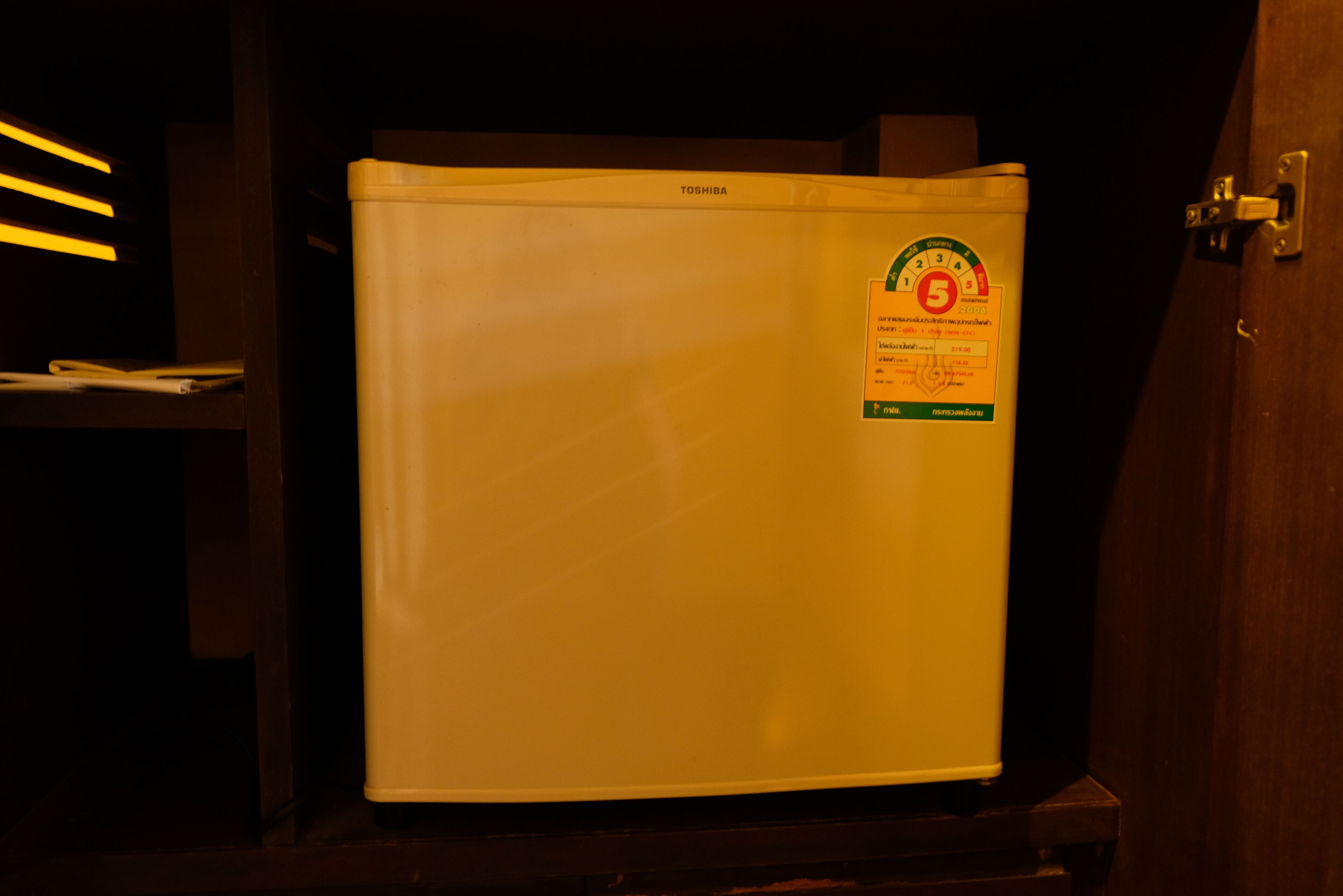 A white refrigerator with a sticker on it, placed in a dimly lit room.