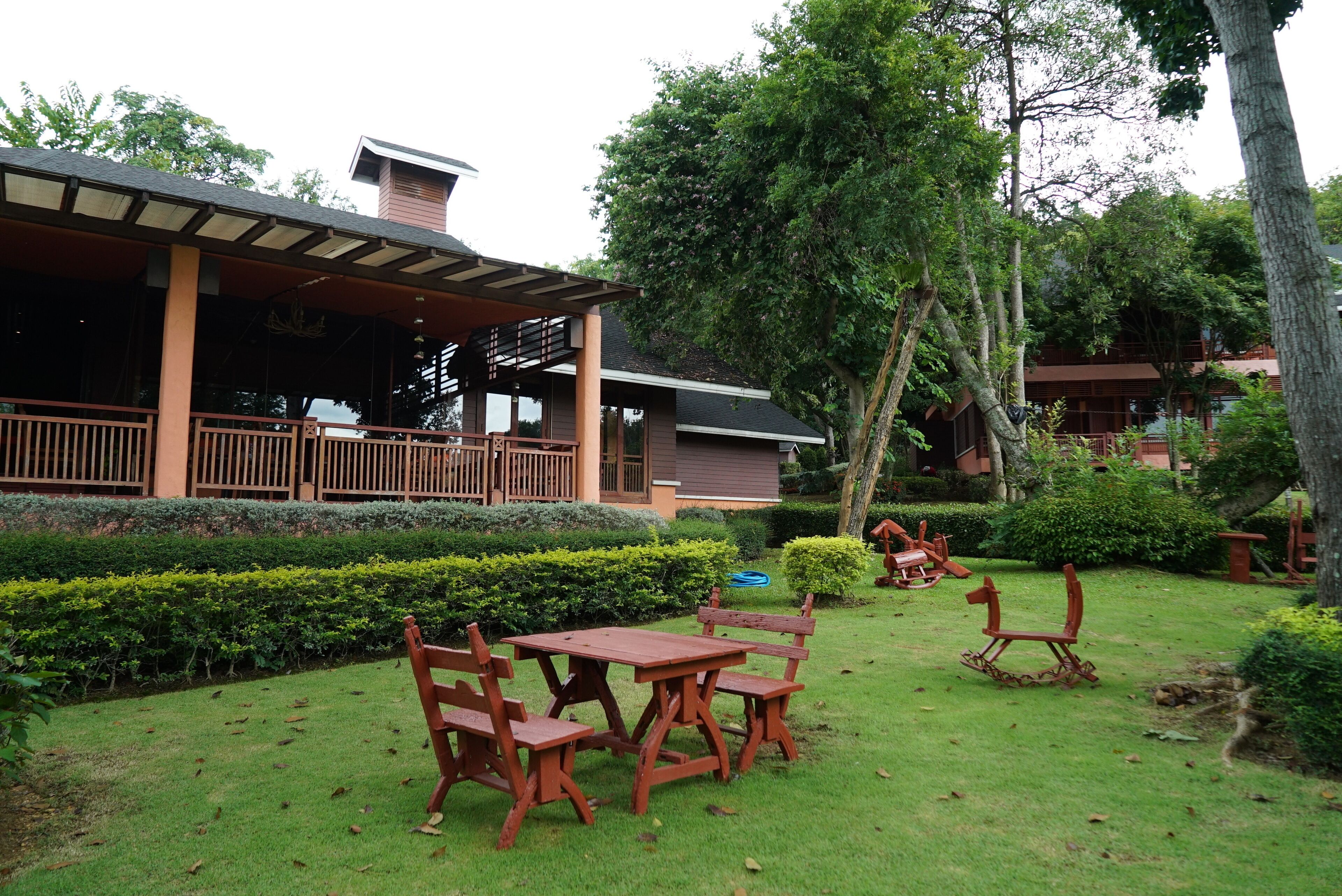 A patio with wooden furniture, a covered seating area, and a well-maintained garden with hedges and trees.