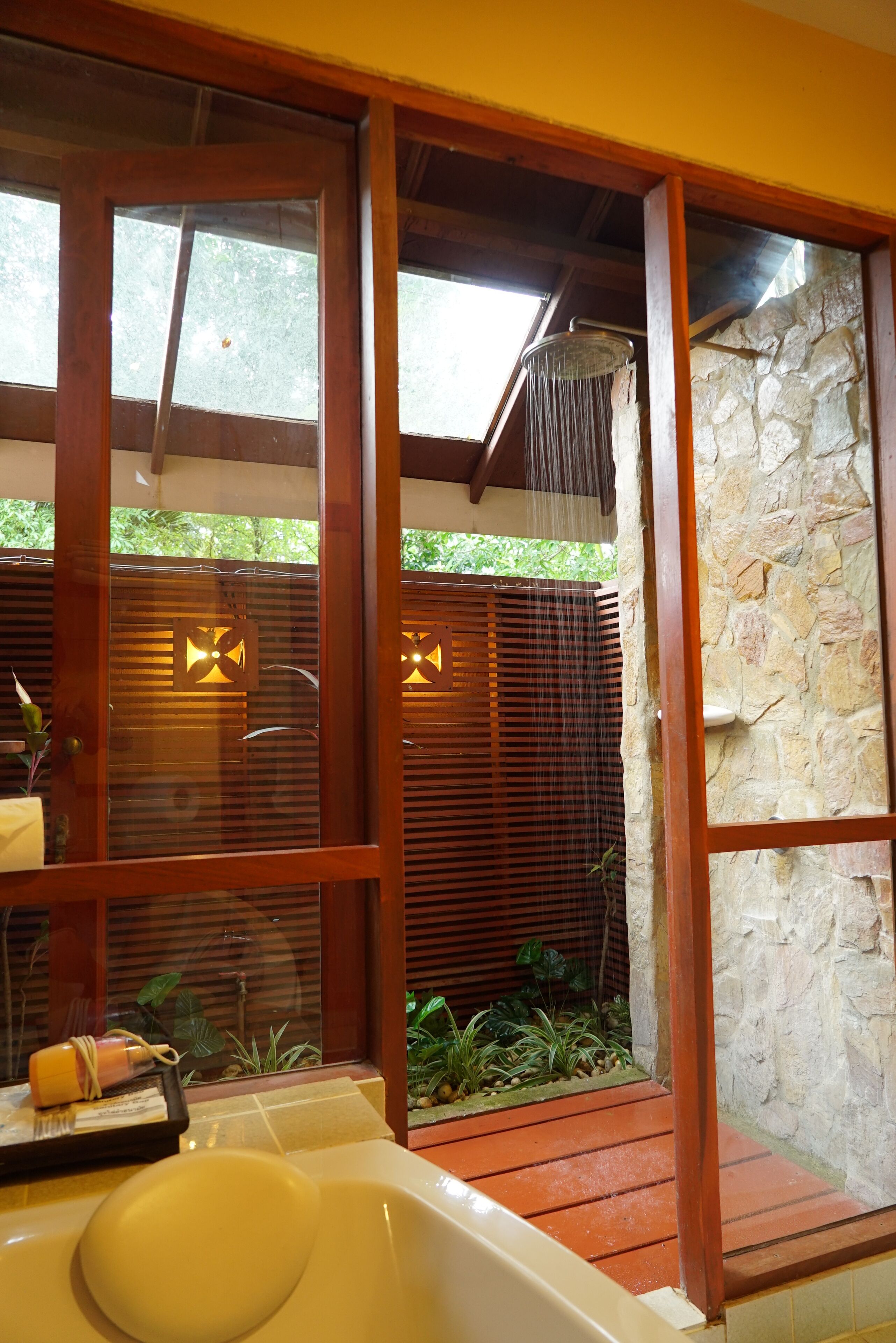 A bathroom with a bathtub, wooden blinds, and a stone wall.
