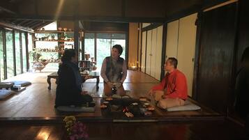 A traditional Japanese room with tatami flooring, a low table with a vase of flowers, and a wooden shelf with various items.