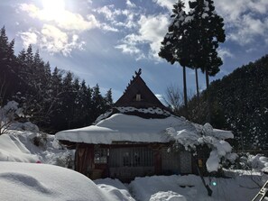 Una cabaña nevada con techo inclinado, rodeada de árboles y un cielo despejado.