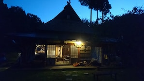 Una casa tradicional con techo de paja, con un interior visible que incluye un comedor, y un cartel que dice "Banya".
