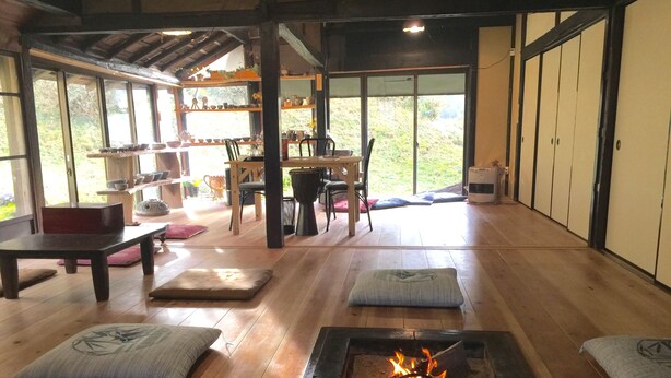Una habitación tradicional japonesa con suelo de tatami, una mesa baja con cojines, una chimenea y vistas del jardín a través de grandes puertas correderas.