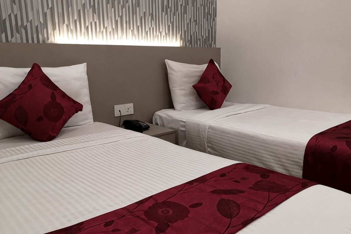 Two single beds with white bedding and red floral-patterned pillows, a nightstand with a phone, and a wall with a geometric pattern.