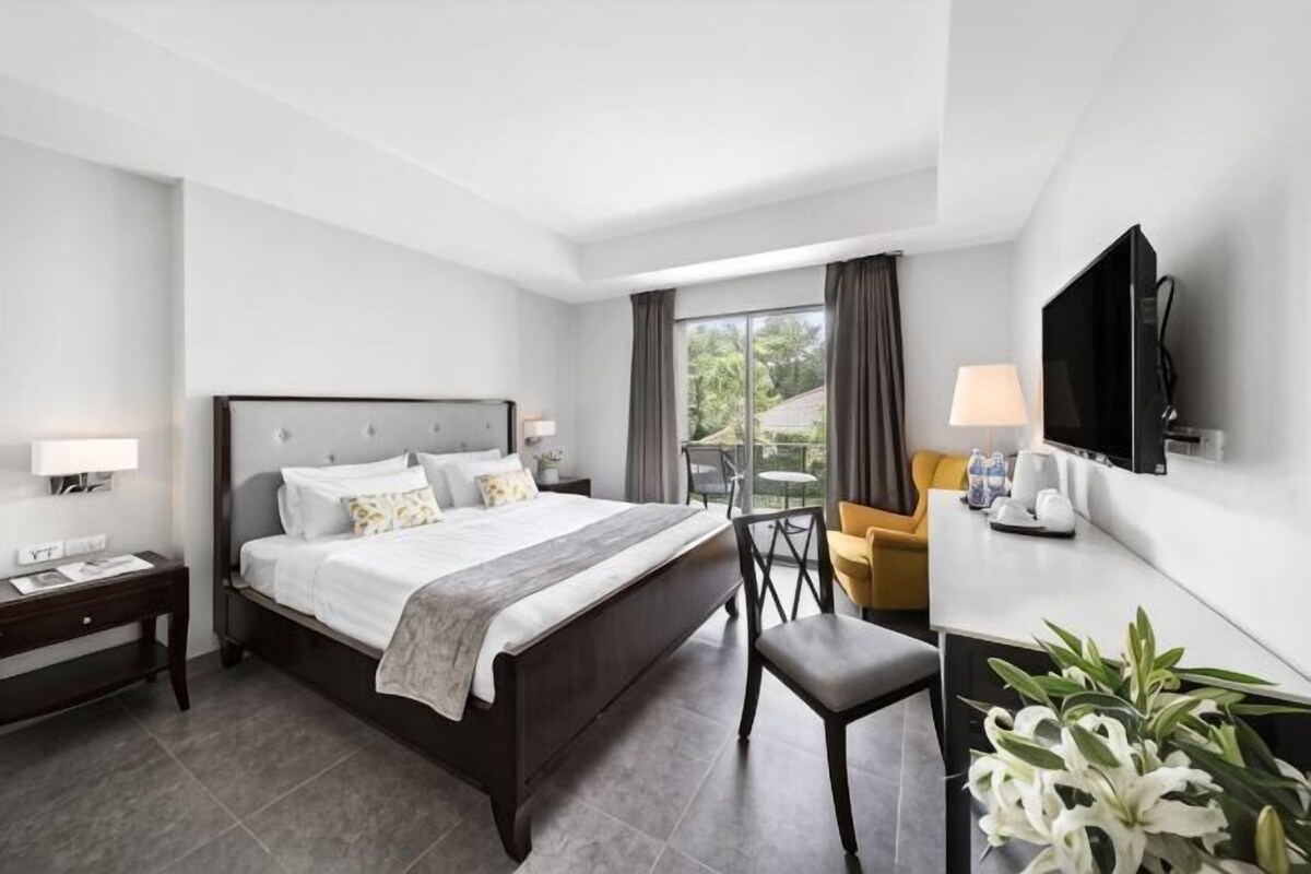 A hotel room with a bed, bedside tables, a TV, a desk, and a chair.