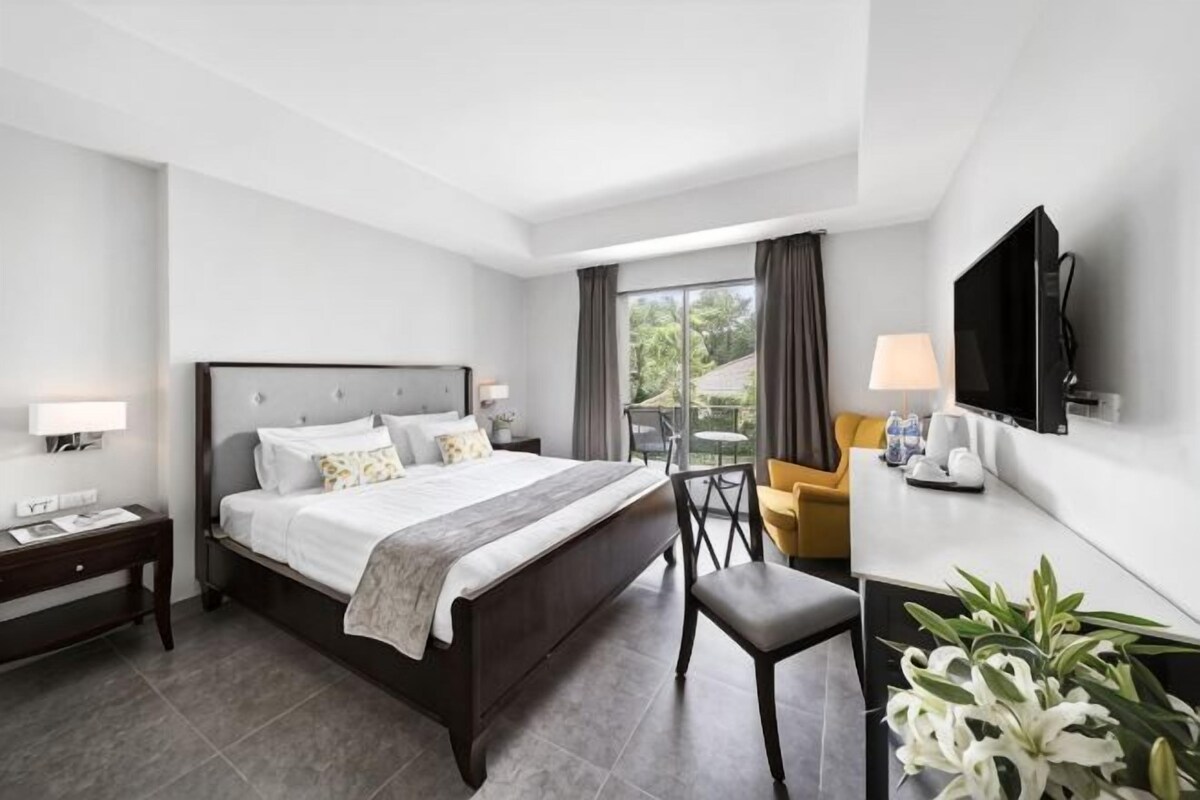 Una habitación de hotel con cama, mesitas de noche, televisor, escritorio y una silla.
