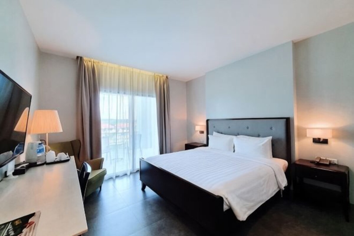 A hotel room with a bed, a desk with a lamp, a chair, a TV, and a window with curtains.