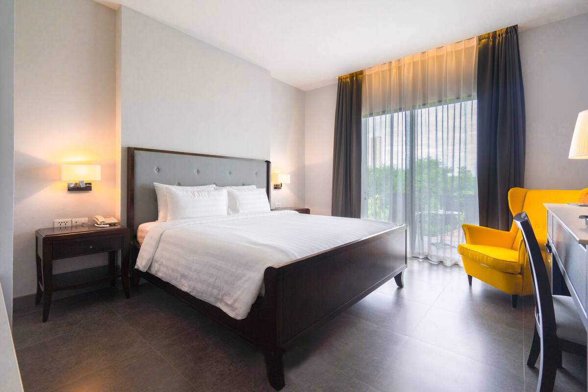 A hotel room with a large bed, a desk, a chair, and a window with curtains.