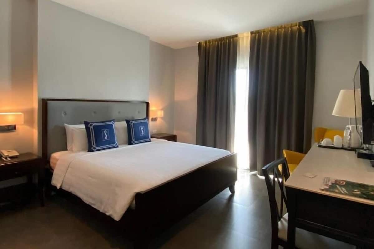 A hotel room with a bed, bedside tables, a desk, and a chair.