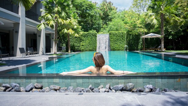 A pool with a person relaxing at the edge, surrounded by palm trees and a stone wall. - The Sala Pattaya (Pattaya)