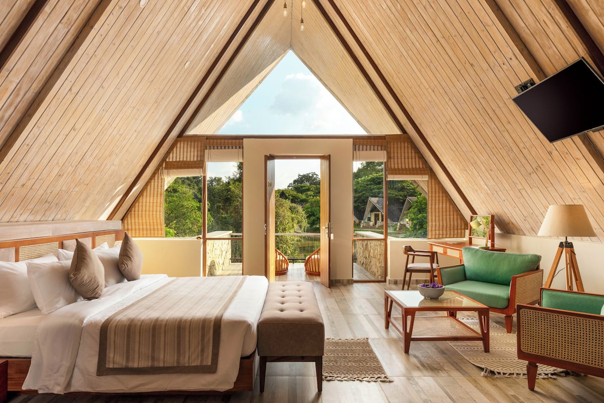 A high-ceilinged, triangular-roofed room with a bed, seating area, and a television.