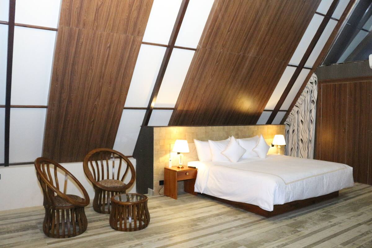 Een slaapkamer met een groot bed, twee nachtkastjes, twee rieten stoelen en een houten plafond.