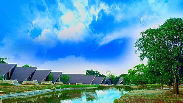 A canal with buildings with sloped roofs, surrounded by greenery and trees. - Liyya Water Villas (Dambulla)