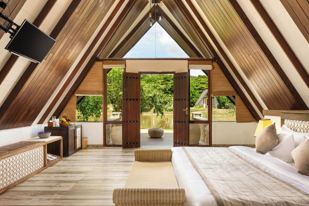 Een kamer met hoge plafonds, een bed, een televisie en uitzicht op groen buiten.