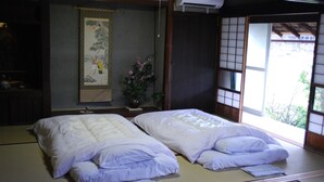 Ett traditionellt japanskt rum med tatamimattor på golvet, två tatamimattor, en shojiskärm, en upphängd rullbild och en vas med blommor.