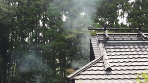 En traditionell byggnad med ett tak täckt av tegelpannor, omgiven av tät skog.