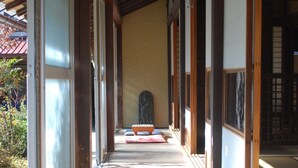 En korridor med träbjälkar och skjutdörrar, som leder till ett rum med tatamimattor och en traditionell japansk staty.