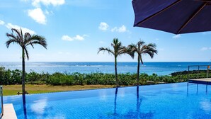 Une magnifique piscine à débordement d’un bleu profond, offrant une vue sur l’océan et les palmiers.