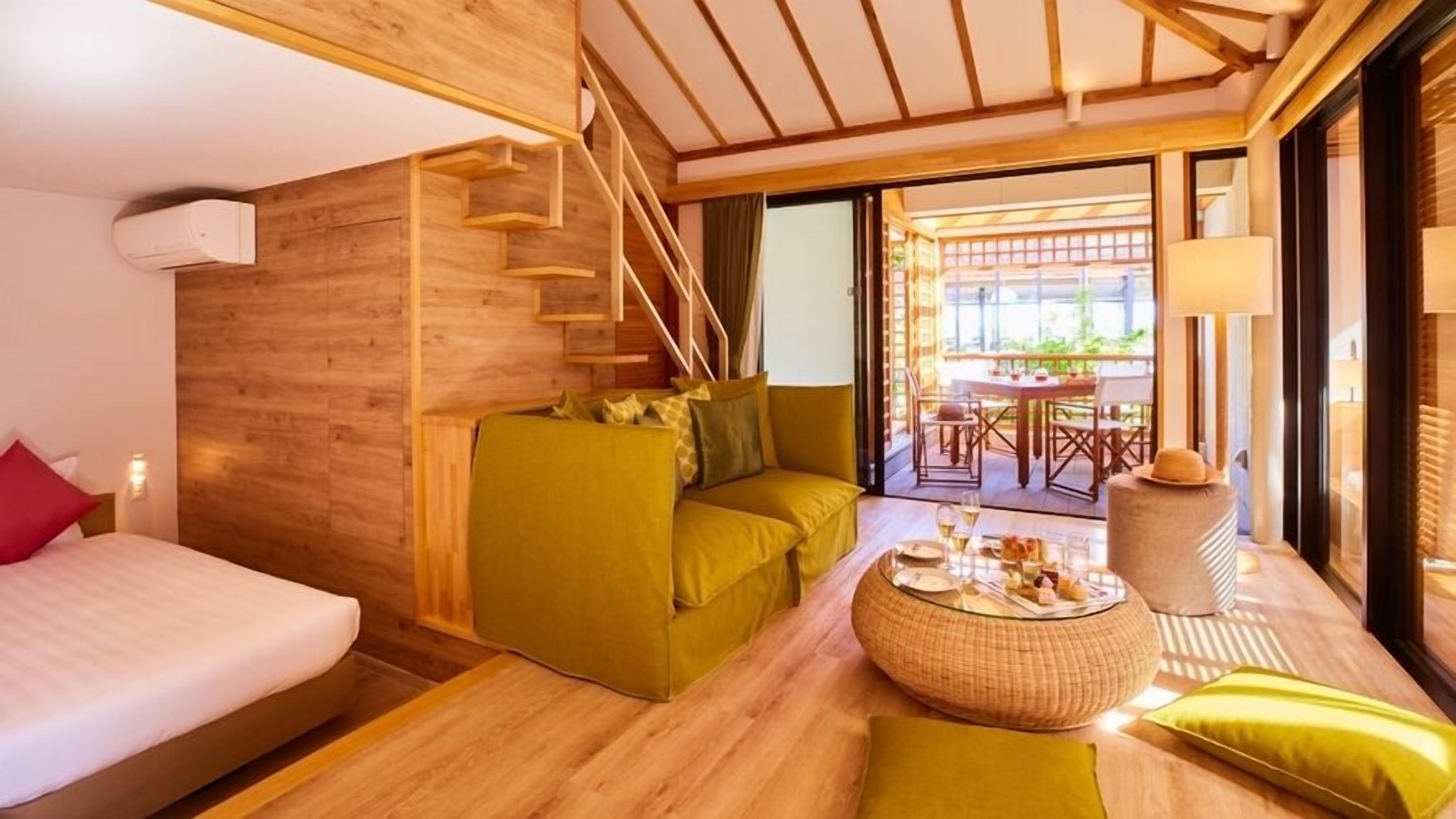 Une chambre d’hôtel moderne avec un intérieur en bois, un canapé, une table à manger avec un plateau en verre et un escalier.