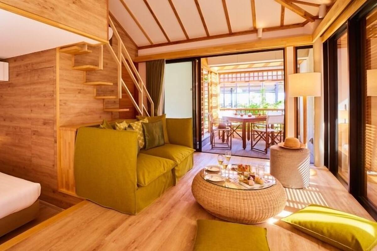 Ein modernes Hotelzimmer mit Holzvertäfelung, einer Couch, einem Esstisch mit Glasplatte und einer Treppe.