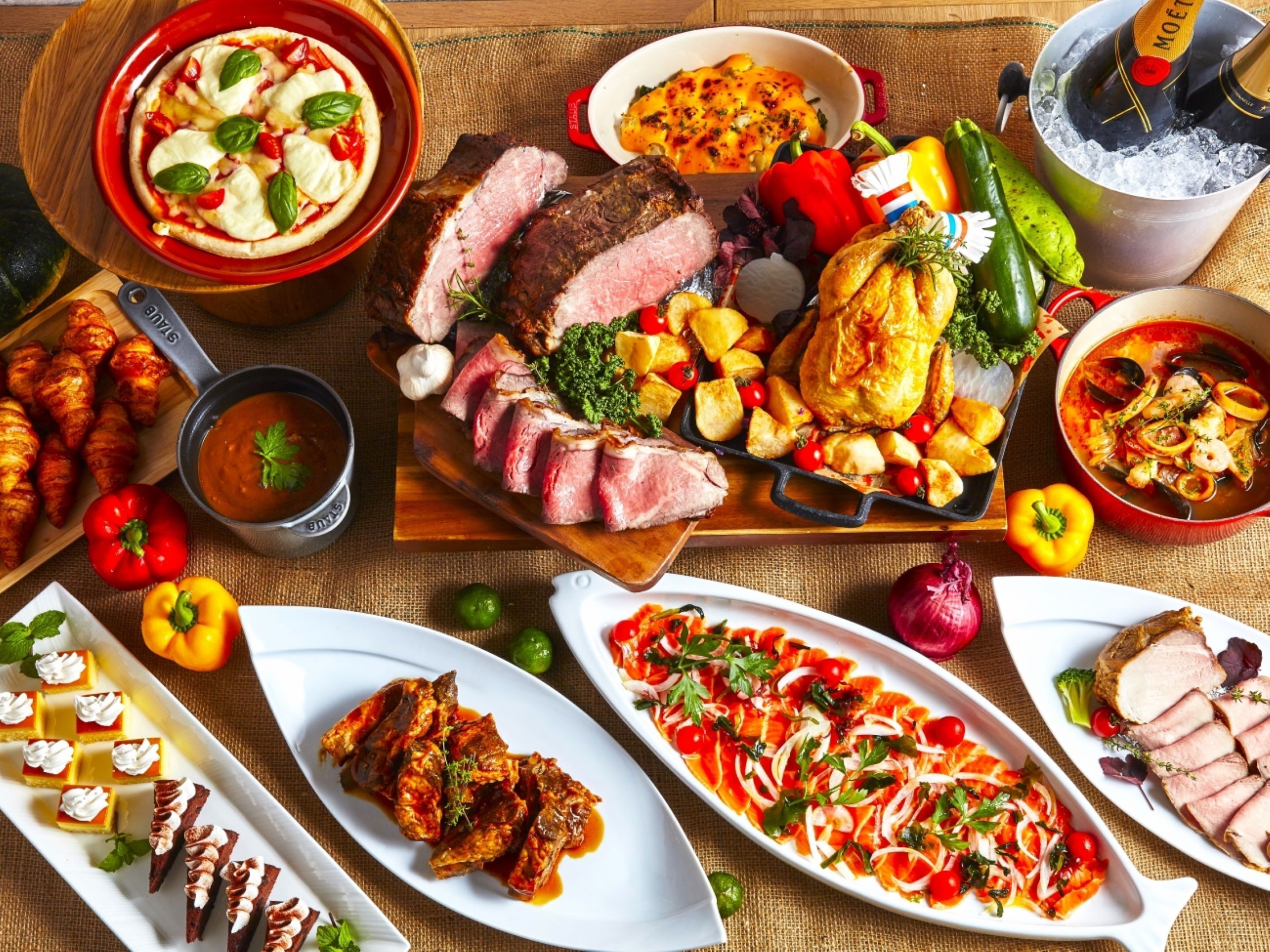 Diversos pratos incluindo carnes assadas, legumes e sobremesas sobre uma mesa de madeira.