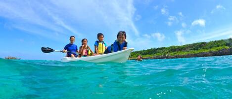 A group of people in a small boat on turquoise water, with a clear sky and a rocky coastline in the background.