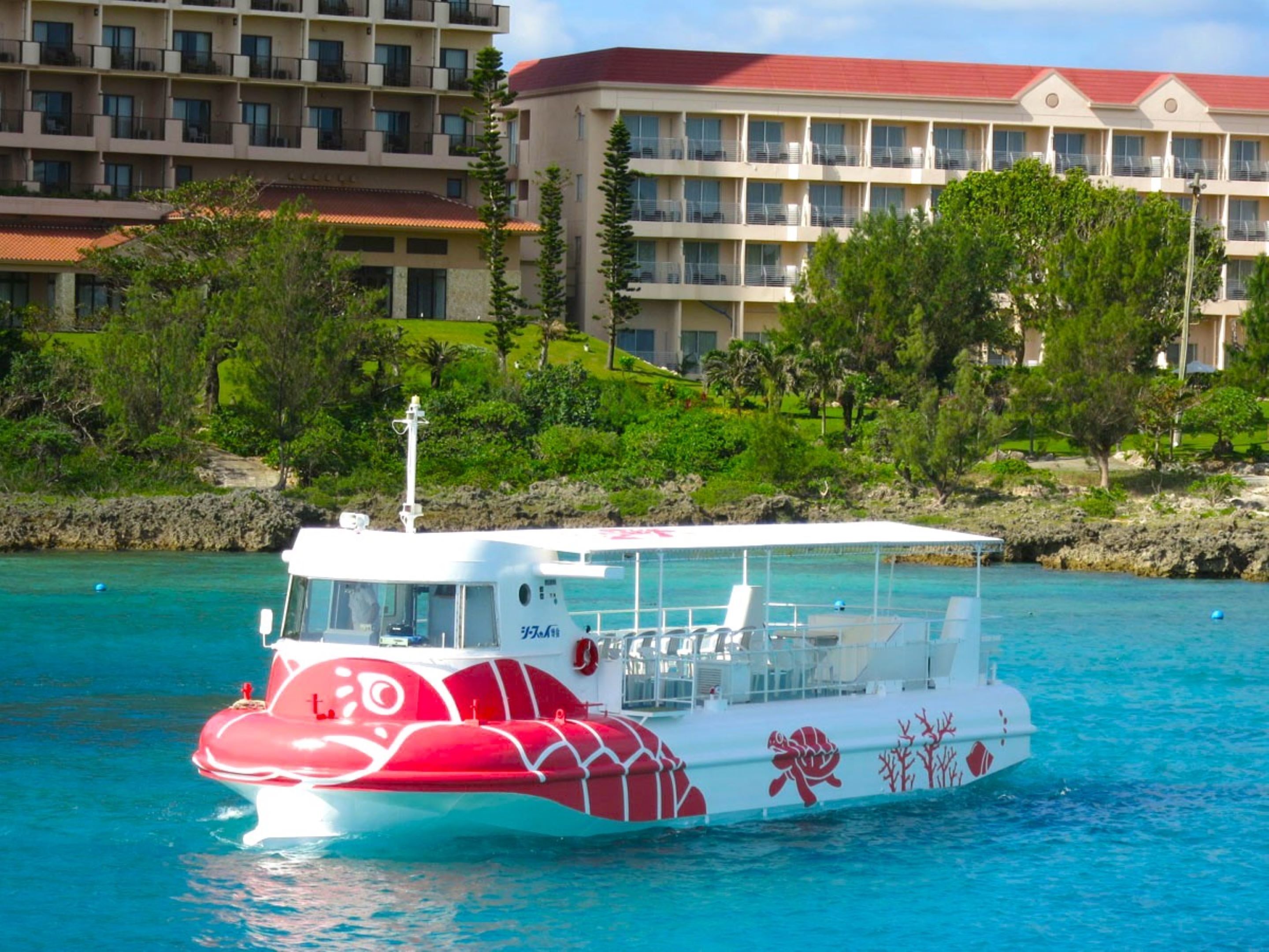 Un bateau aux couleurs rouge et blanc était amarré près d’un hôtel doté de nombreux balcons et d’un toit rouge.