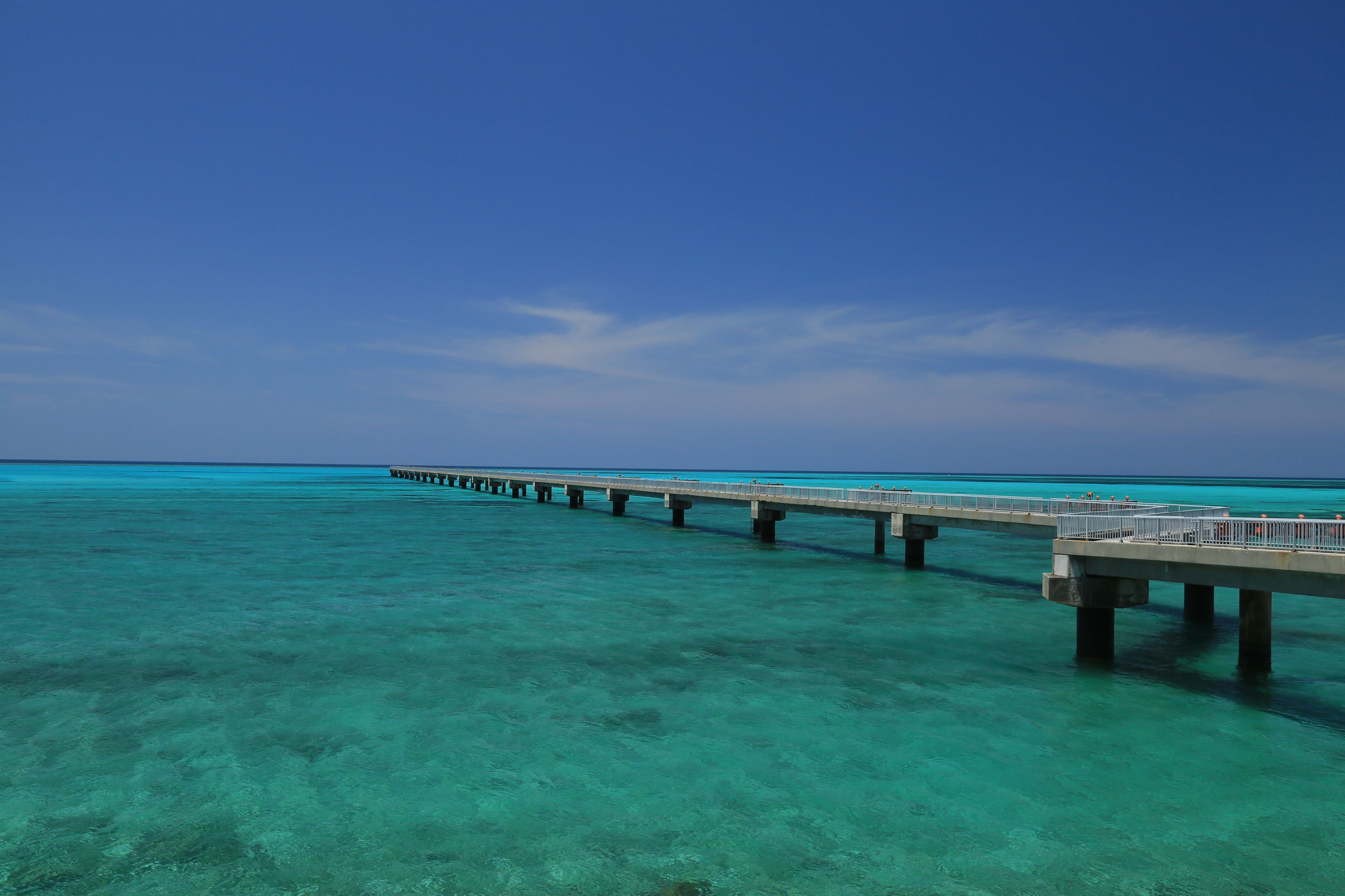 A pier extending into a clear turquoise sea under a bright blue sky.