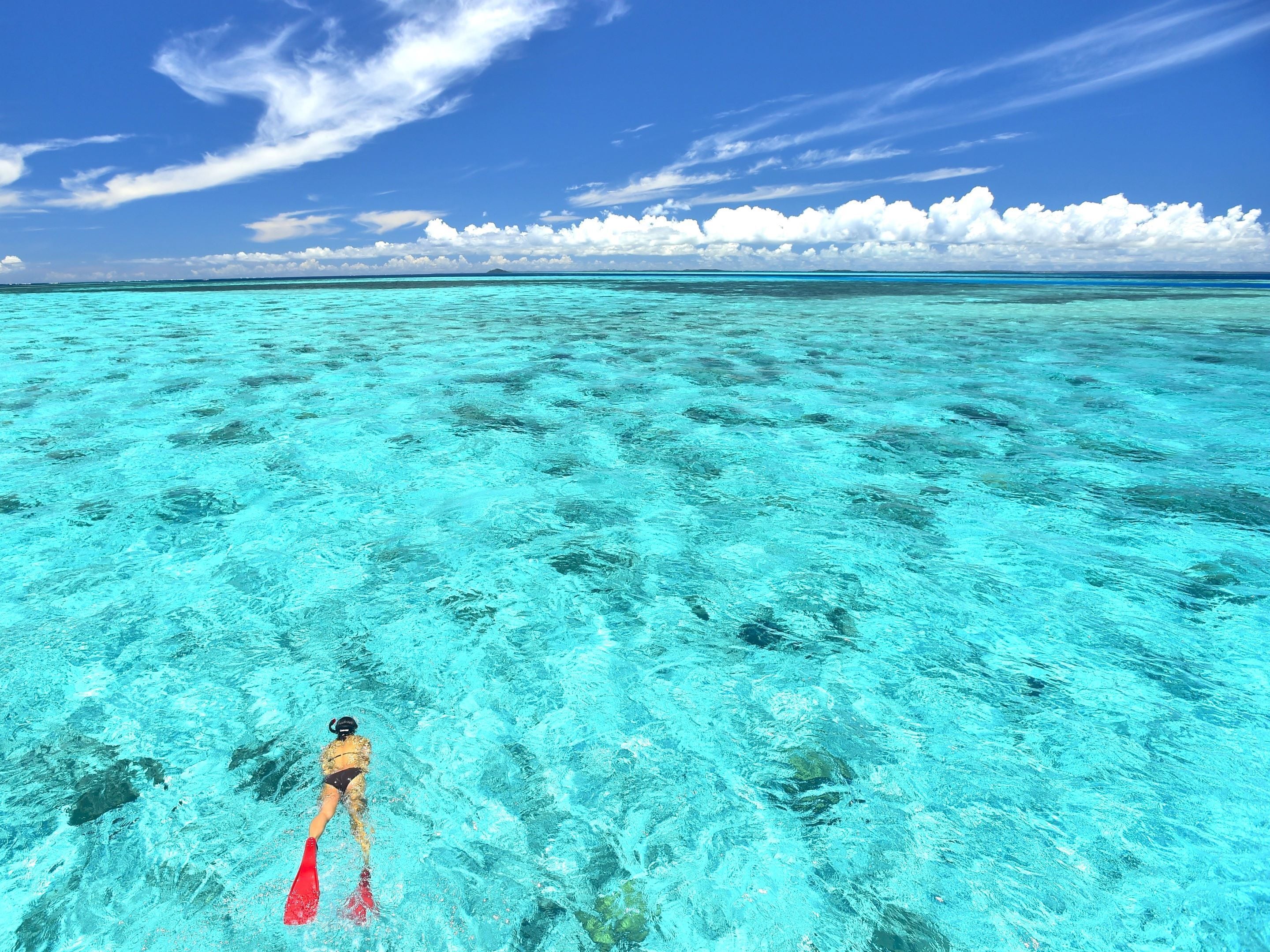 Une personne faisant de la plongée avec tuba dans une eau turquoise et limpide, avec un horizon lointain et des nuages.