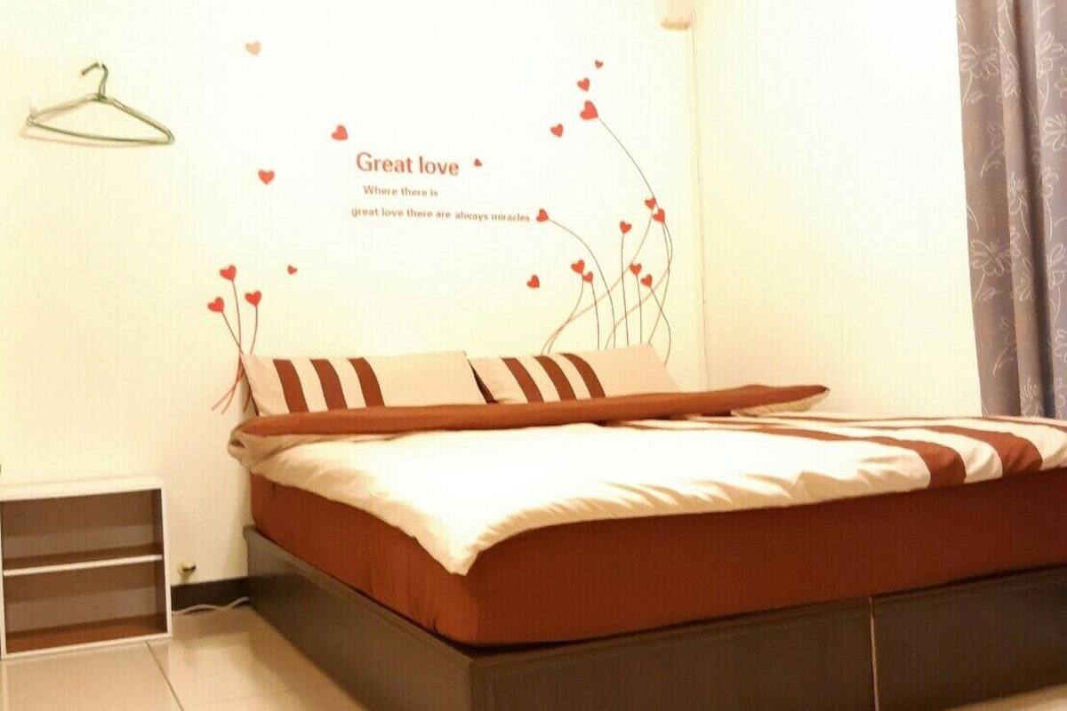 A bedroom with a bed, a wall decoration, a hanger, and a window with curtains.