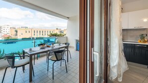 Ein Balkon mit Esstisch und Stühlen, Blick auf einen Swimmingpool und einen Ausblick auf die Stadt.